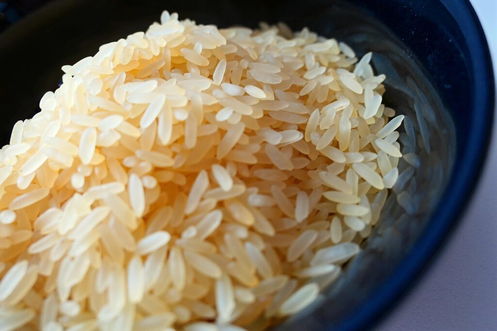 Pile of uncooked white rice grains in a dark bowl, close-up view emphasizing texture and shape of individual grains